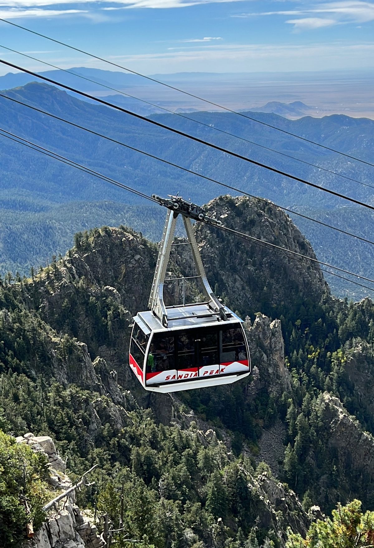 A gondola is flying over a mountain with mountains in the background.