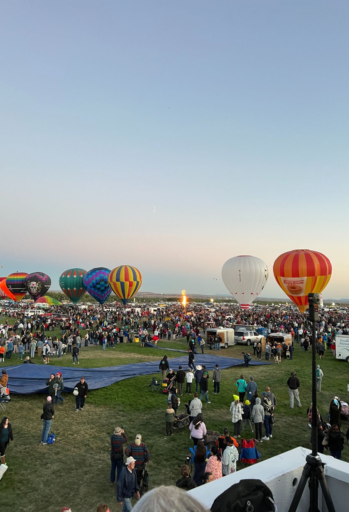 A group of people watching a large group of hot air balloons.