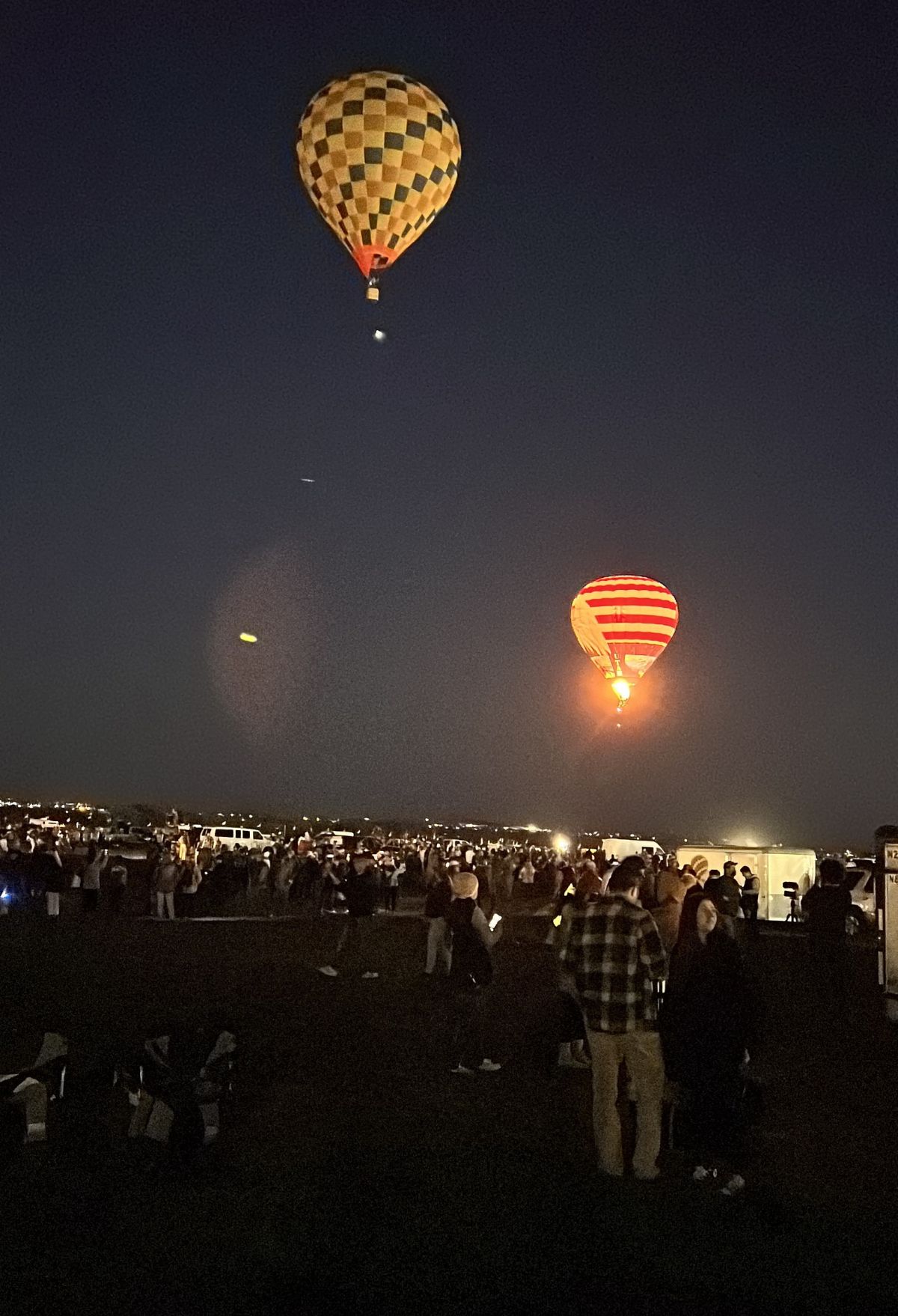Balloon festival attendees marvel at hot air balloons illuminated at night.
