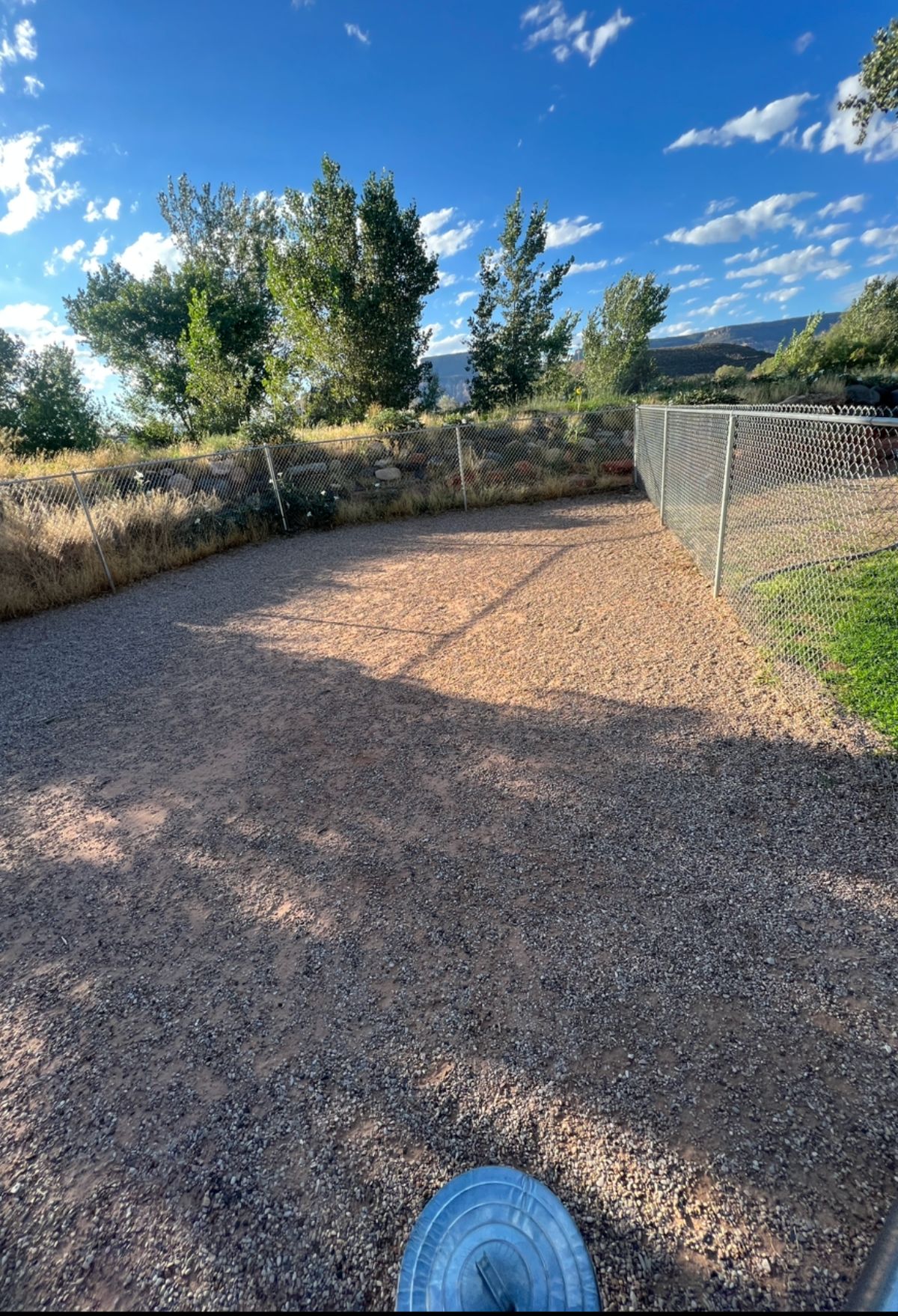 A gravel dog park with a fence in the background.