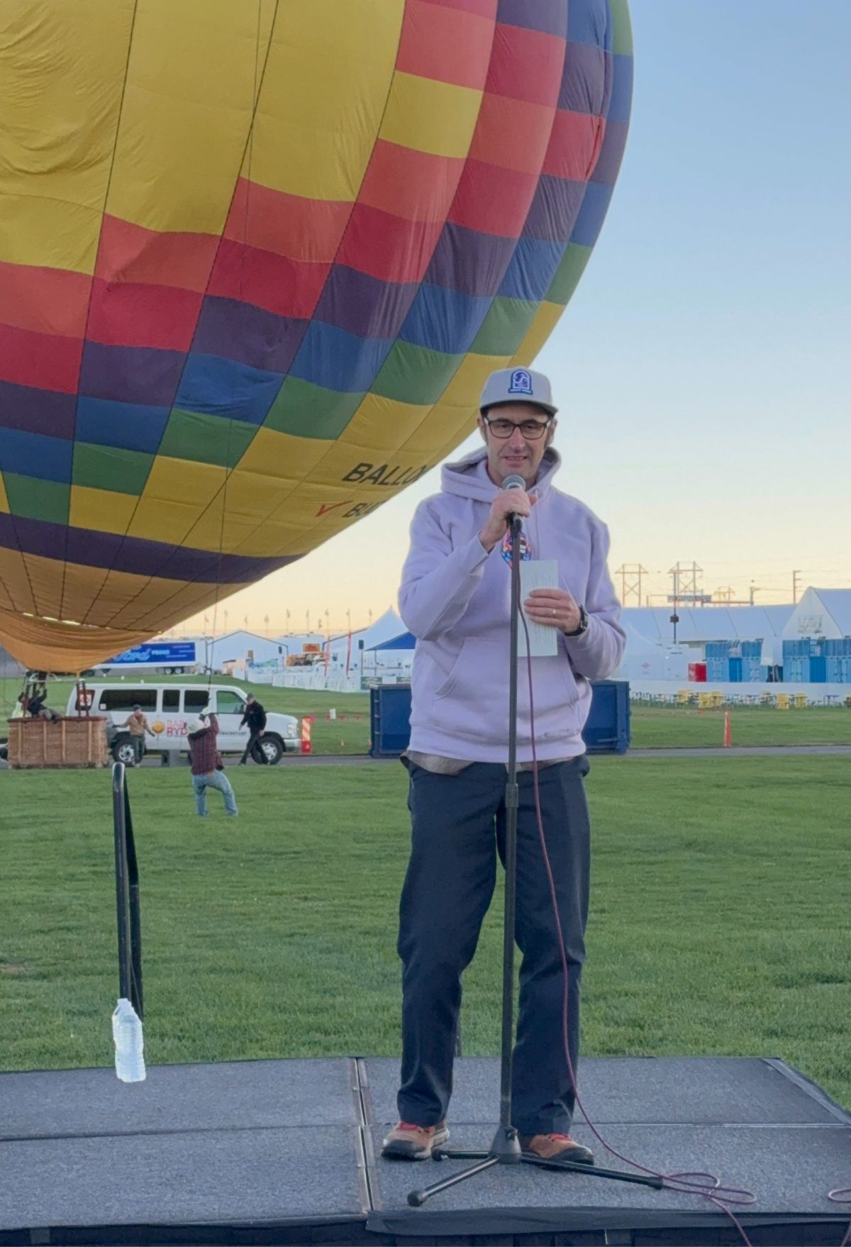 A man standing on a stage in front of a Meow Wolf Skyworm hot air balloon.