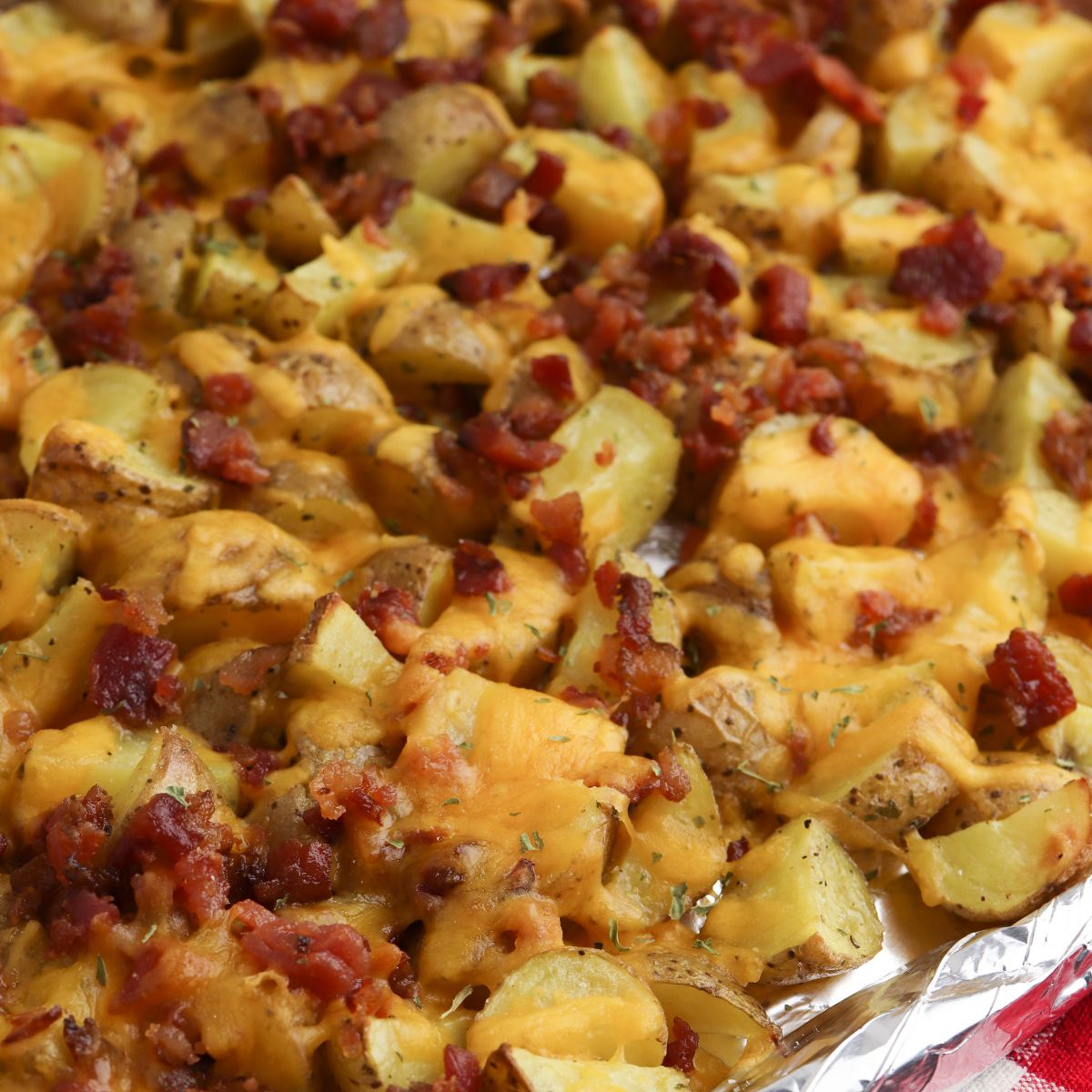 A tray of roasted potatoes topped with melted cheese, bacon bits, and herbs.