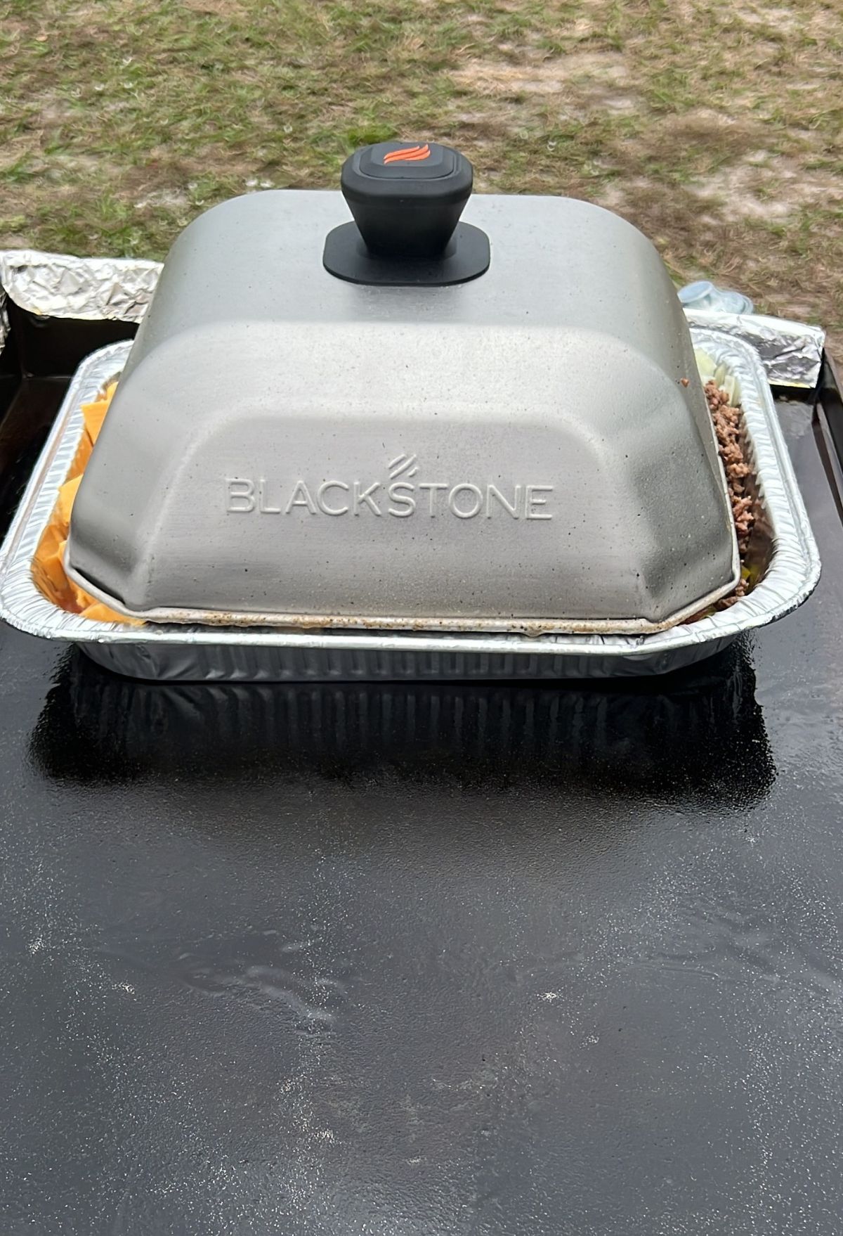 Covered Blackstone griddle on a metal tray outdoors, resting on a black surface.
