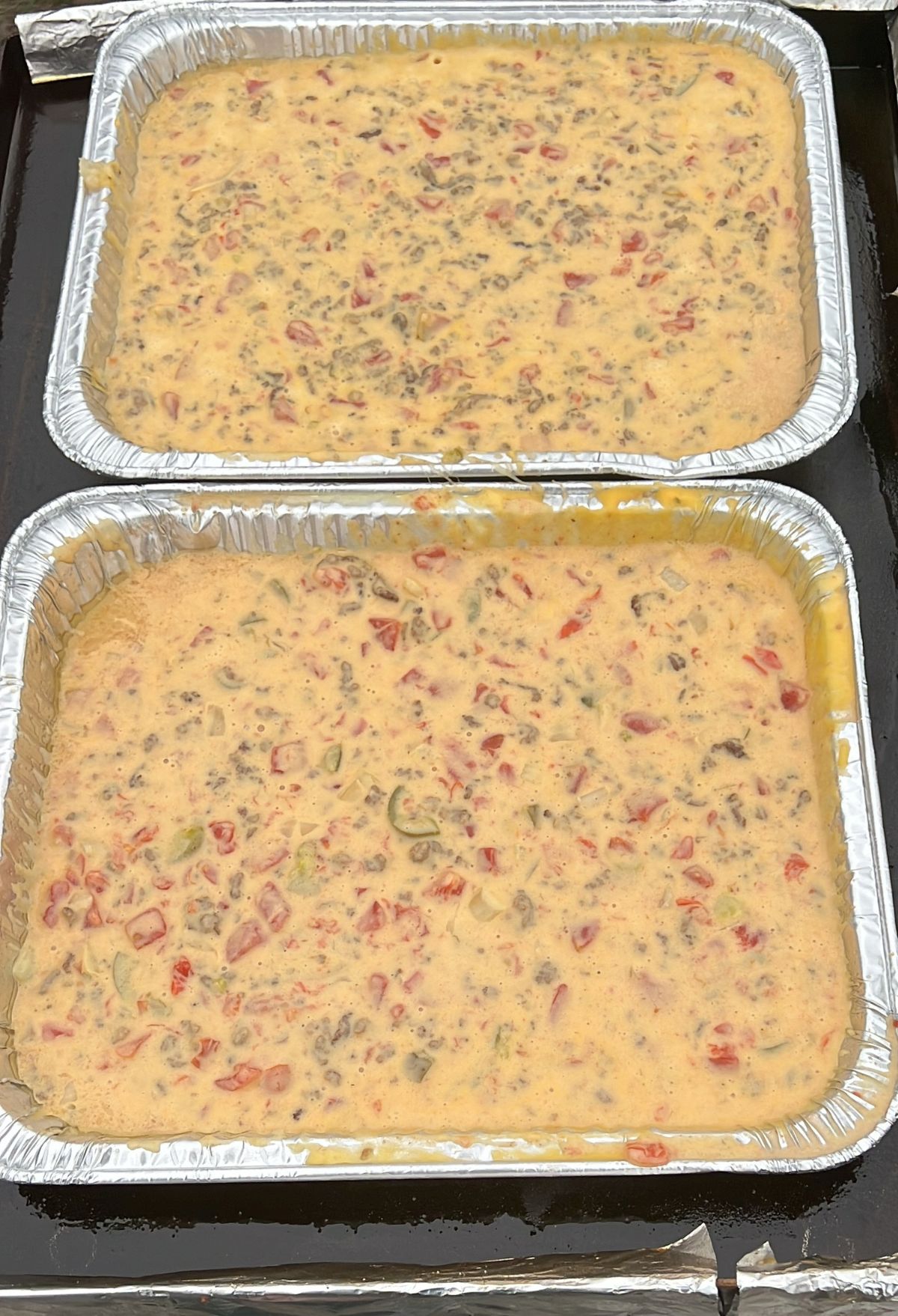Two foil pans filled with a mixture of cheese, ground meat, and diced tomatoes, uncooked.