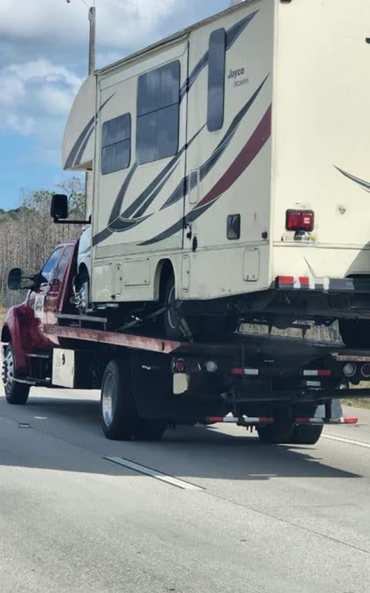 A flatbed tow truck is transporting a Jayco camper on a multi-lane road during the day—perfect for those dreaming of living full-time in an RV.