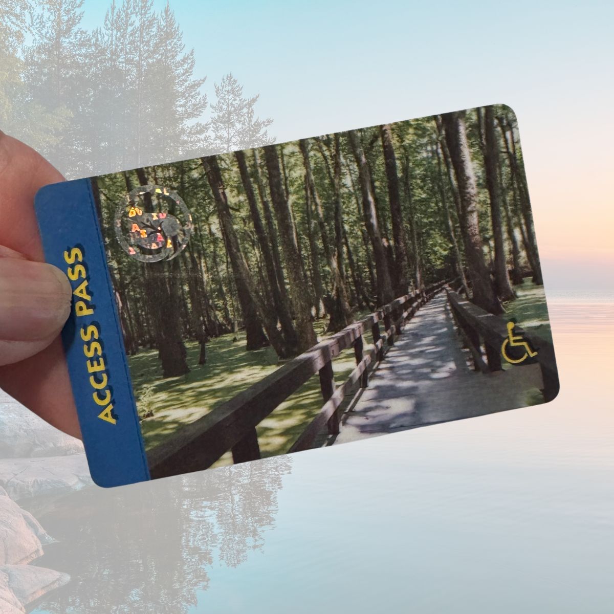 A hand holds a "national parks pass" card featuring an image of a wooden path through a forest with a wheelchair accessibility symbol.