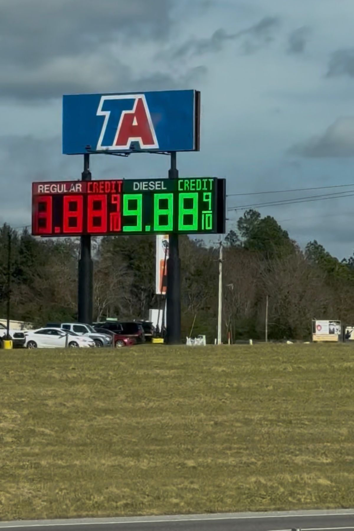 Gas station price sign showing Regular Credit at $3.89⁹ and Diesel Credit at $9.98⁹, with TA logo above on a partly cloudy day, highlighting RV fuel costs for travelers passing through.