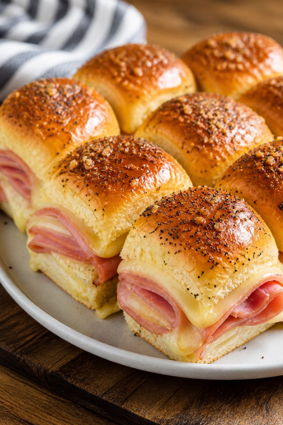 A plate of ham and cheese sliders made with soft, golden-brown buns, sprinkled with seasoning—perfect for easy and delicious RV camping meals.