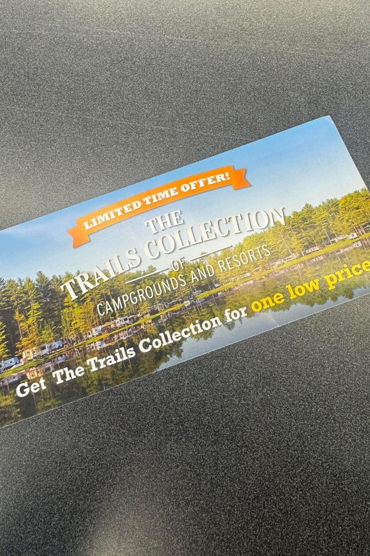 A flyer on a gray surface advertises "The Trails Collection of Campgrounds and Resorts," featuring a lakeside campground, a "Limited Time Offer" banner, and promotes Thousand Trails memberships.