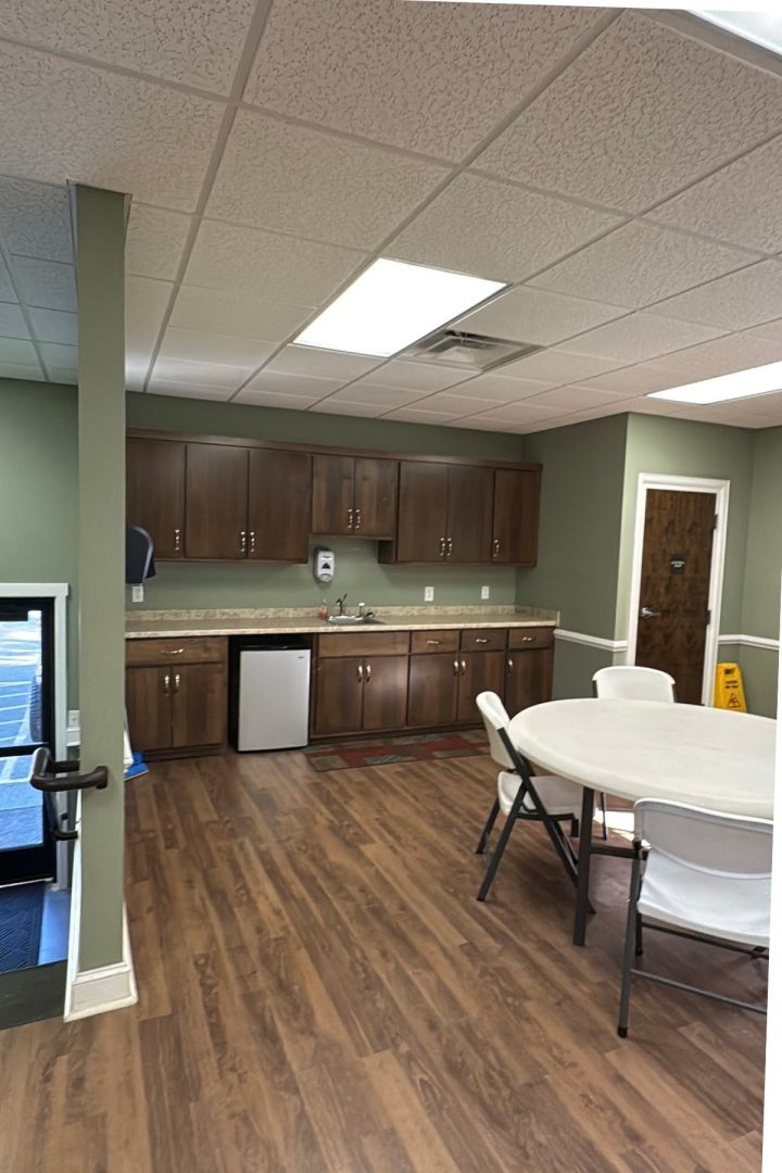 Break room with wood flooring, round table and chairs, small kitchenette with sink, cabinets, mini fridge, and a paper towel dispenser—ideal for relaxing at Green Mountain Thousand Trails.