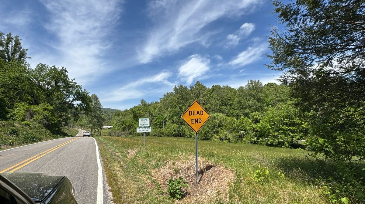 A rural road with a yellow "Dead End" sign beside it; trees and greenery surround the area under a partly cloudy blue sky near Green Mountain Thousand Trails.