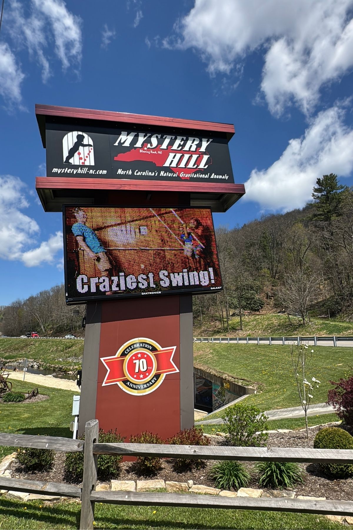 Outdoor sign for Mystery Hill in North Carolina, near Green Mountain Thousand Trails, features a digital image of two people on a swing with "Craziest Swing!" and highlights the attraction's 70th anniversary.