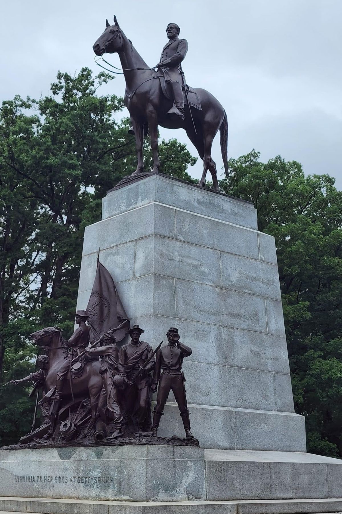 Bronze equestrian statue atop a large stone pedestal, with additional bronze figures of soldiers and a flag at the base, surrounded by trees—a striking tribute as the semiquincentennial approaches.