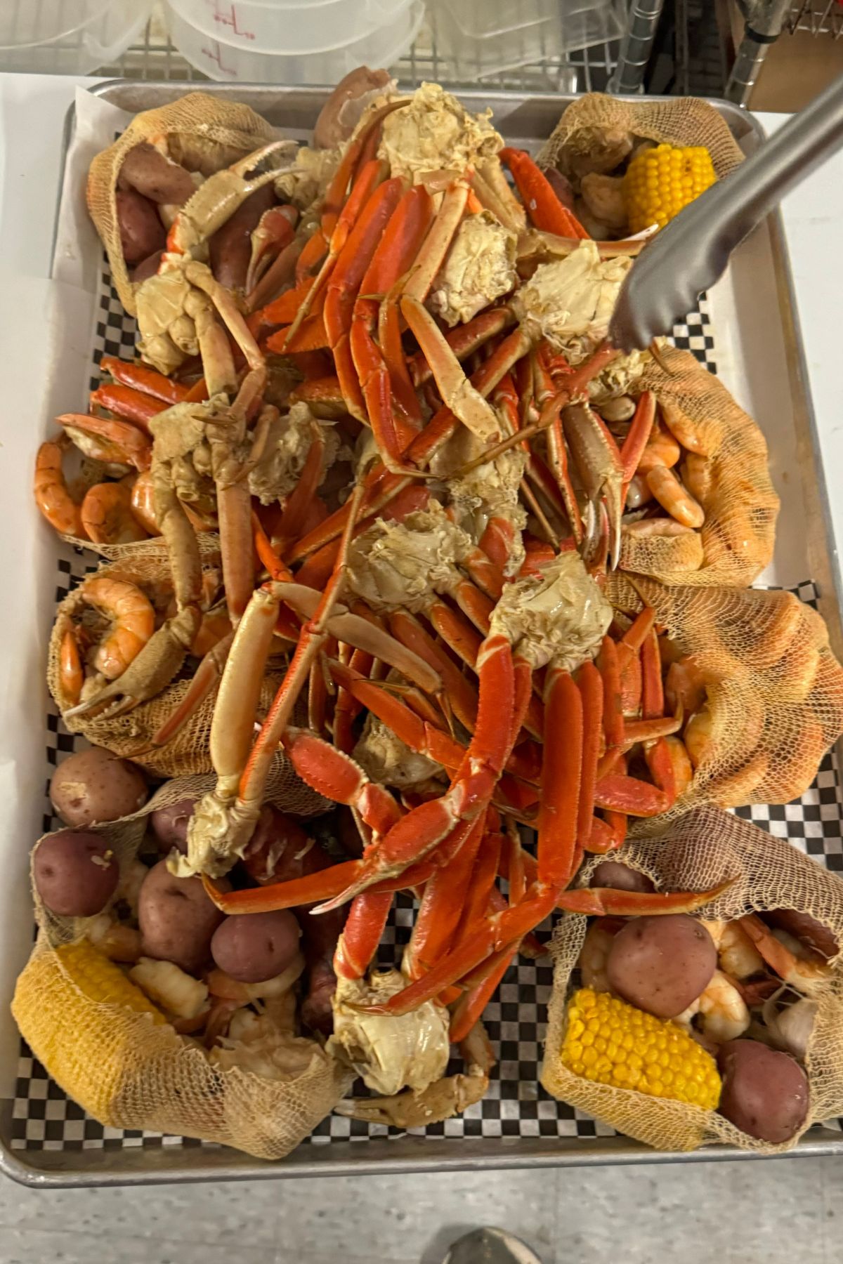 A tray filled with crab legs, shrimp, red potatoes, corn on the cob, and netted bags containing more seafood and vegetables brings a taste of Southeast Kansas to your table.