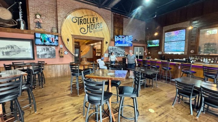 Spacious Southeast Kansas restaurant with wooden floors, high ceilings, and a large "Trolley House" sign on the wall; several tables, a bar area, and a few people standing and seated.
