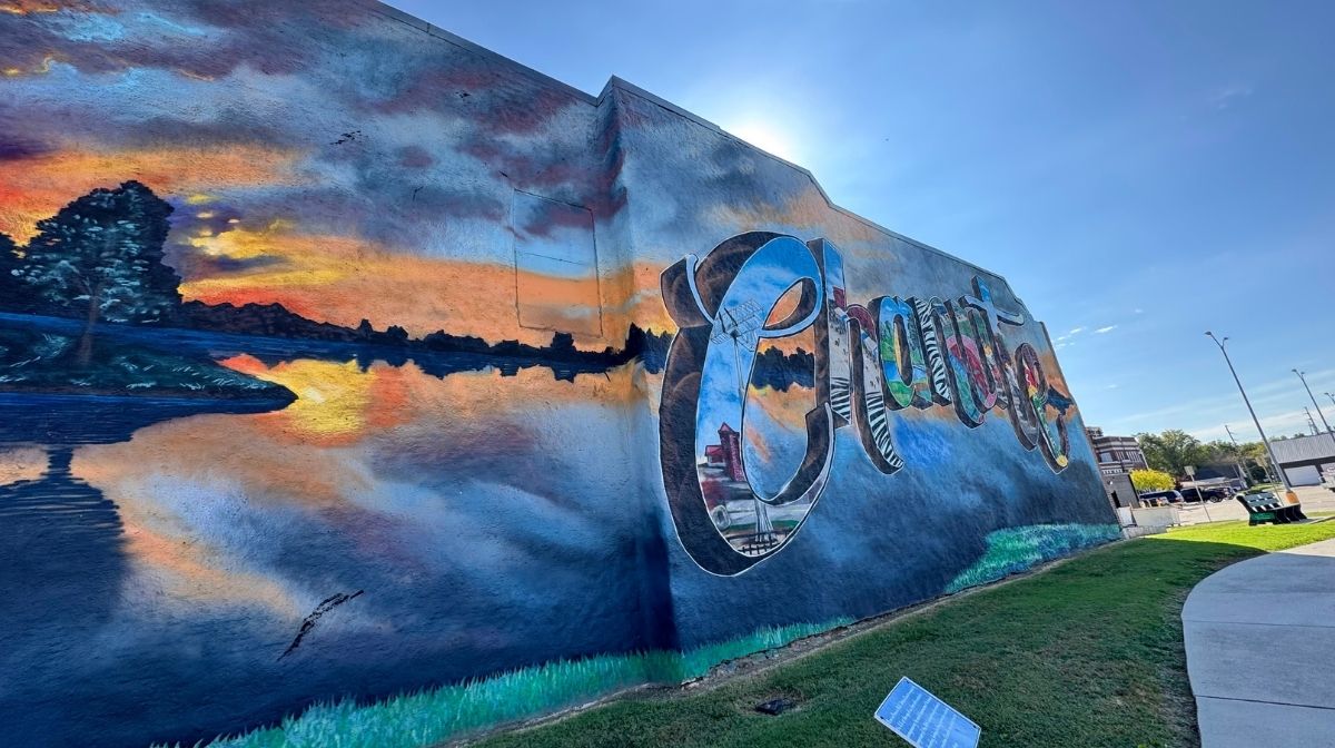 A colorful mural on a building wall in Southeast Kansas depicts a sunset over water and features the word "Change" in large, reflective letters.