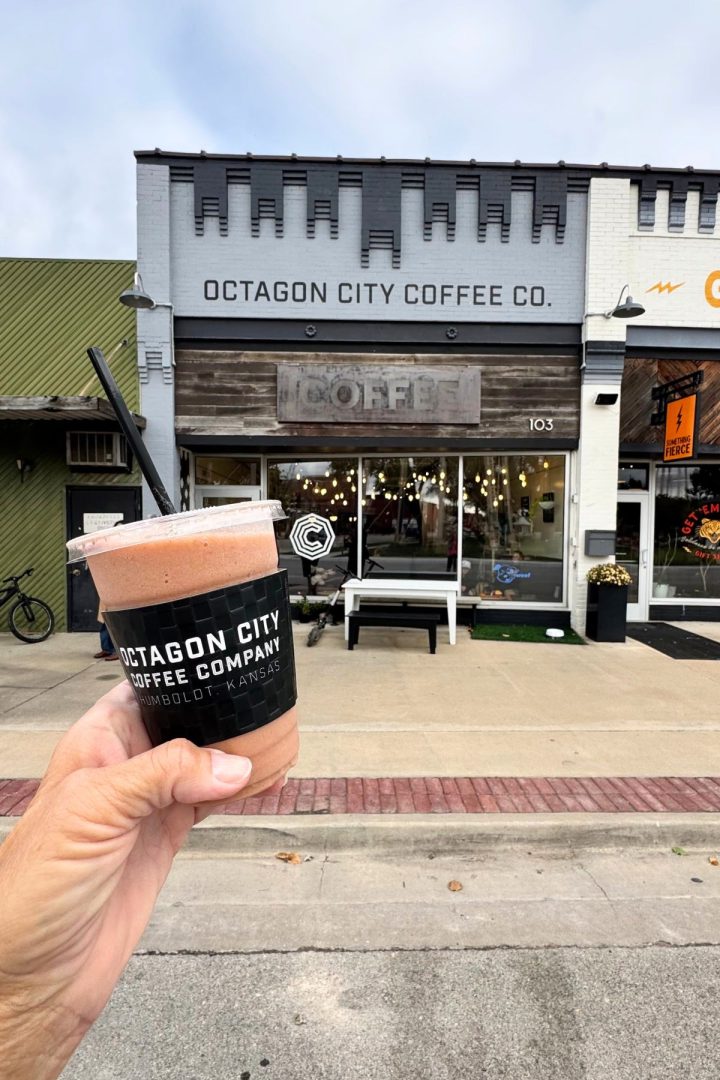 A hand holds a smoothie cup labeled “Octagon City Coffee Company” outside the storefront of Octagon City Coffee Co., a local favorite in Southeast Kansas’s Humboldt.