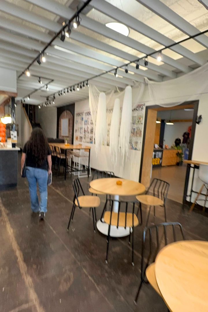 A person walks through a cozy Southeast Kansas cafe with round wooden tables and Halloween ghost decorations hanging from the ceiling.