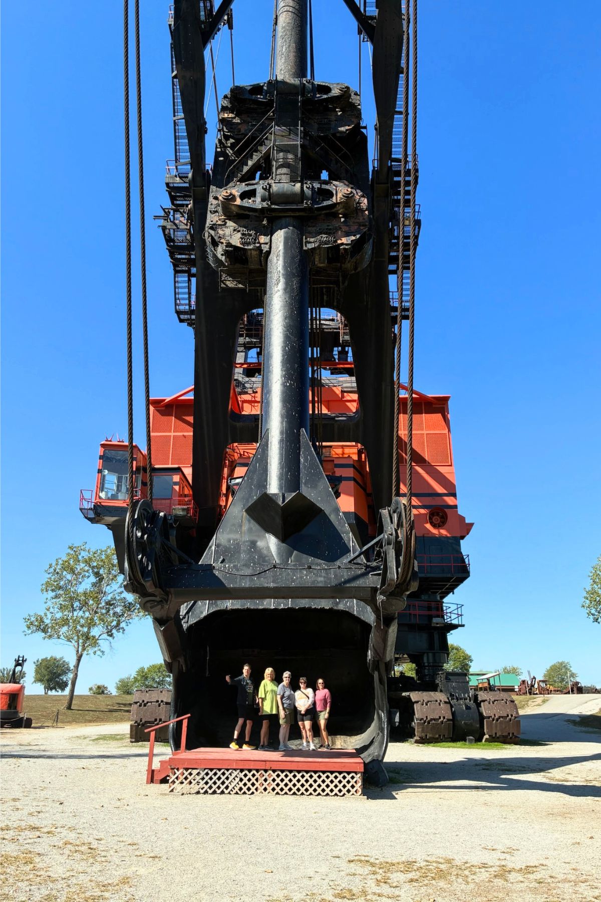 A group of people stands inside the bucket of a massive mining excavator on display in Southeast Kansas under a clear blue sky. Big Brutus.