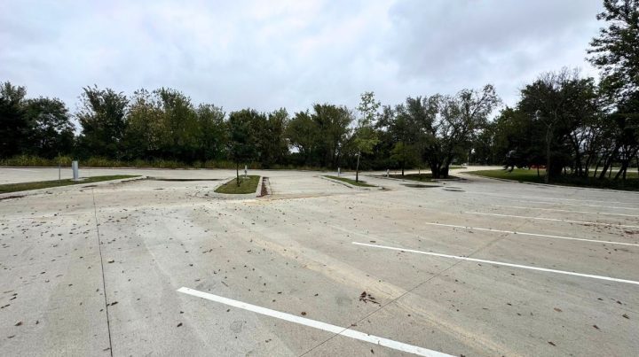 Empty concrete parking lot with white painted lines, scattered leaves, and trees in the background under a cloudy Southeast Kansas sky.