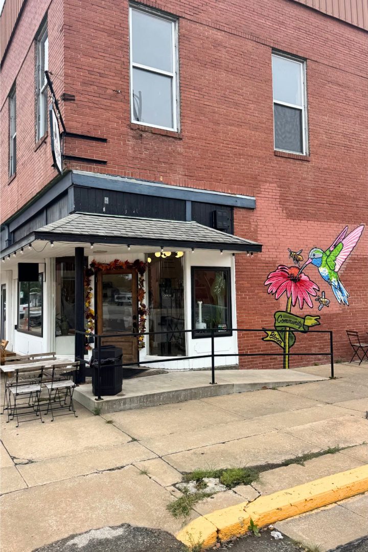 A corner brick building in Southeast Kansas with a small café, outdoor seating, and a mural of a hummingbird and flower on the side wall.