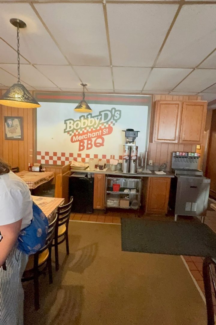 Interior of a Southeast Kansas BBQ restaurant featuring wooden paneling, a soda fountain, drink dispensers, and a large Bobby D's Merchant St. BBQ sign on the wall.