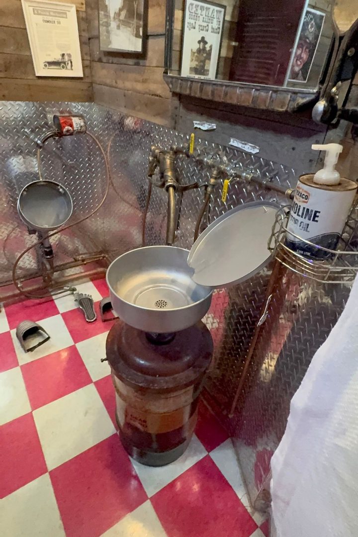 Metal wash station in a retro-themed room with red and white checkered floor, diamond plate walls, and vintage decor—including a Texaco hand cleaner dispenser—evoking the classic charm of Southeast Kansas service stations.