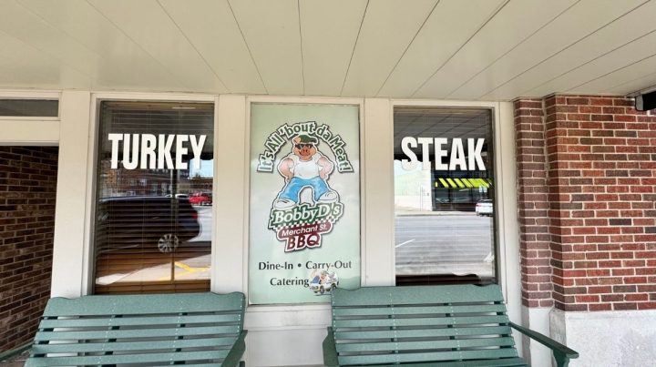 Front of a restaurant with large windows labeled "Turkey" and "Steak," featuring a Bobby D's BBQ sign advertising dine-in, carry-out, and catering. Two green benches sit out front at this Southeast Kansas favorite.