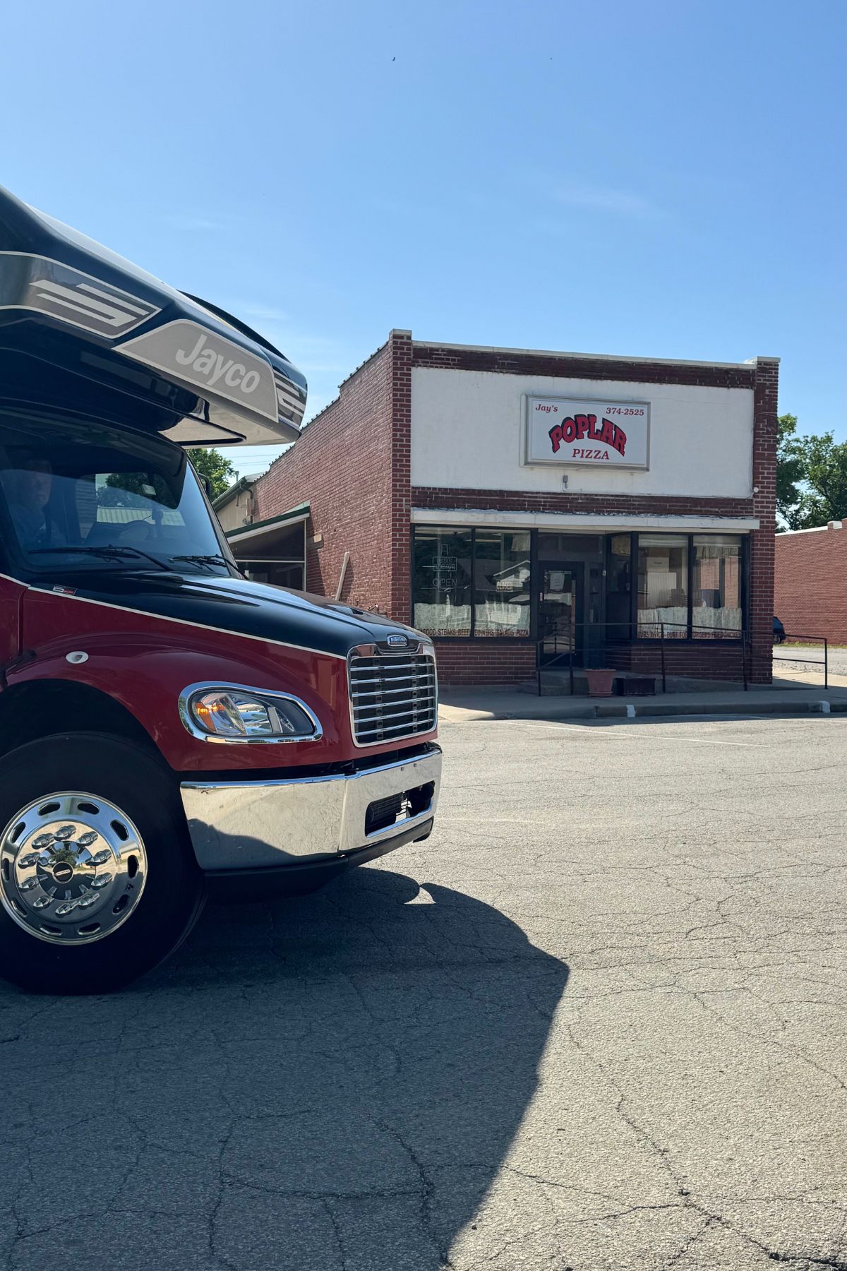 A red Jayco RV is parked in front of Poplin’s Pizza, a small brick restaurant with a blank white sign under the clear blue Southeast Kansas sky.