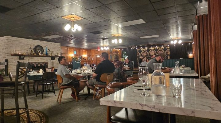 A dimly lit Southeast Kansas restaurant with several diners seated at tables, marble tabletops, decorative lighting, and eclectic wall decor.