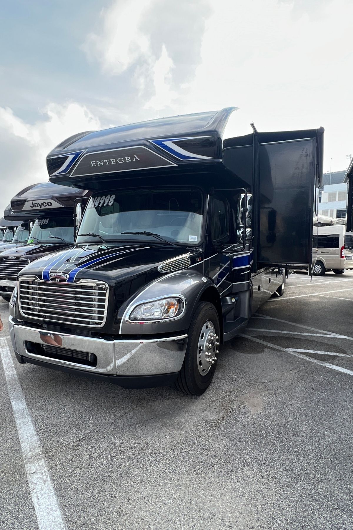 A black Entegra motorhome with extended slide-outs is parked in a lot on a cloudy day, with other RVs visible in the background—a perfect scene for anyone looking to buy an RV and explore the open road in style.