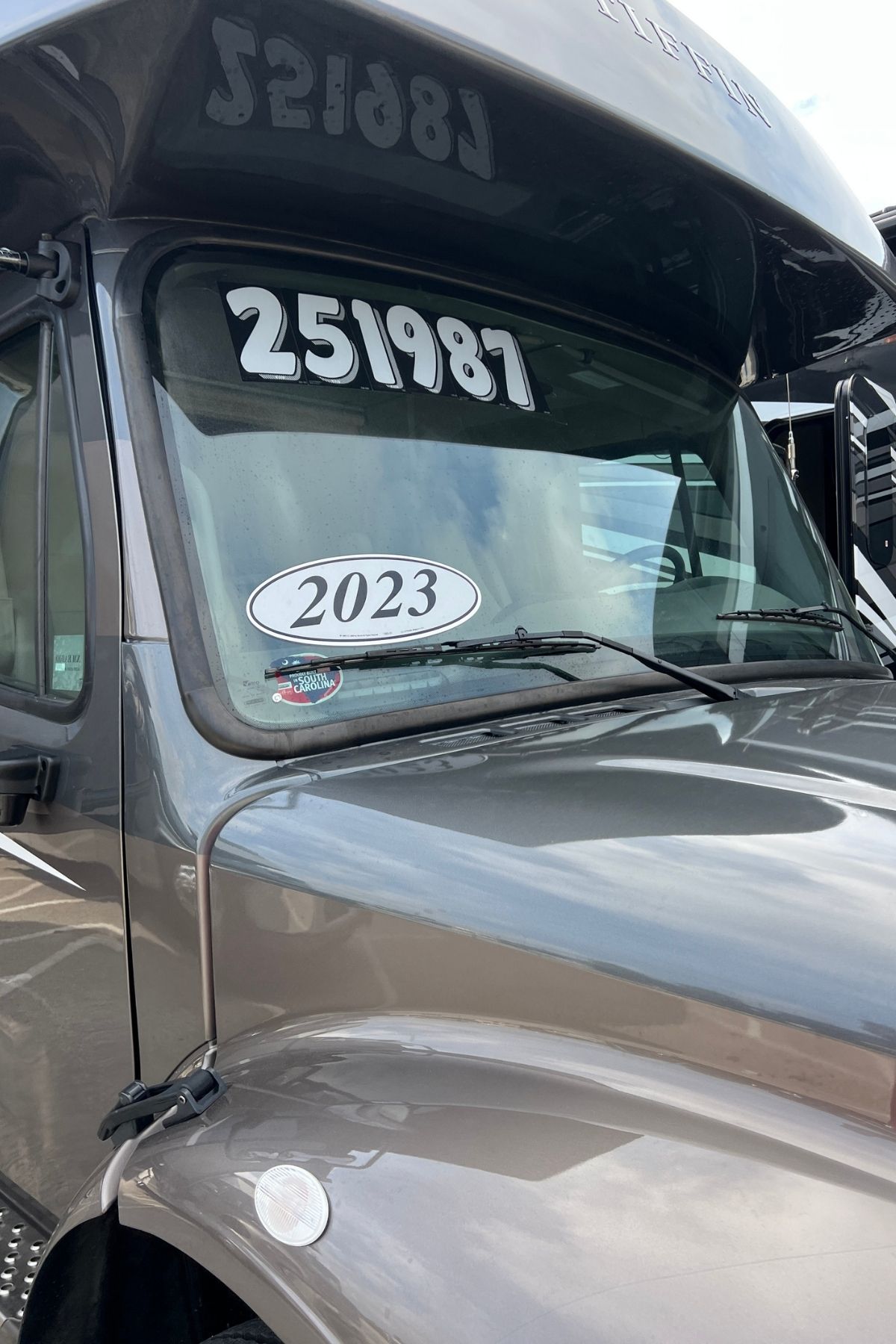 Front of a gray vehicle displaying the numbers “251987” and a “2023” sticker on the windshield, photographed in a parking lot—a great spot to check out if you’re looking to buy an RV.